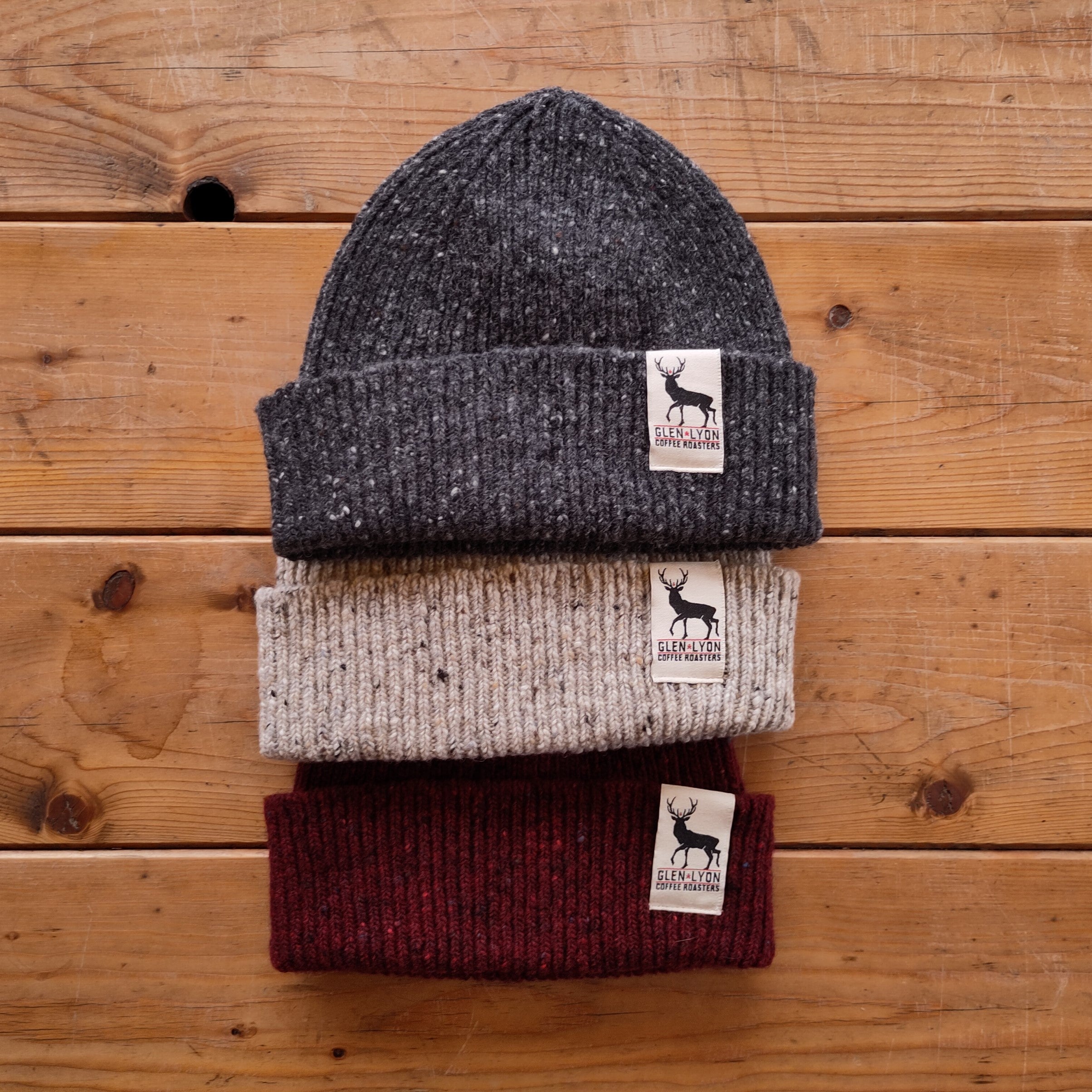 Three Glen Lyon Coffee beanies in different colours lined up overlapping on a wooden table